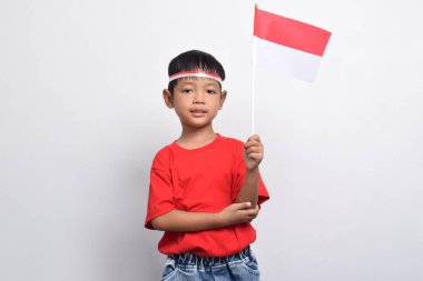 Kırmızı tişörtlü neşeli bir Endonezyalı beyaz arka planda izole edilmiş bir bayrak ve gülümseme taşıyor. Endonezya Bağımsızlık Günü konsepti.