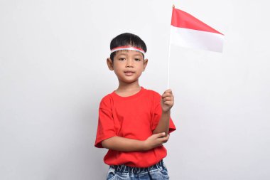 Kırmızı tişörtlü neşeli bir Endonezyalı beyaz arka planda izole edilmiş bir bayrak ve gülümseme taşıyor. Endonezya Bağımsızlık Günü konsepti.