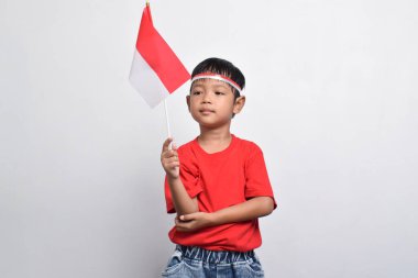 Kırmızı tişörtlü neşeli bir Endonezyalı beyaz arka planda izole edilmiş bir bayrak ve gülümseme taşıyor. Endonezya Bağımsızlık Günü konsepti.