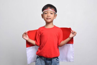 Beyaz arka planda izole edilmiş, arkasında Endonezya bayrağı taşıyan neşeli bir Asyalı çocuk. Endonezya Bağımsızlık Günü konsepti.