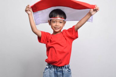Beyaz arka planda izole edilmiş, arkasında Endonezya bayrağı taşıyan neşeli bir Asyalı çocuk. Endonezya Bağımsızlık Günü konsepti.