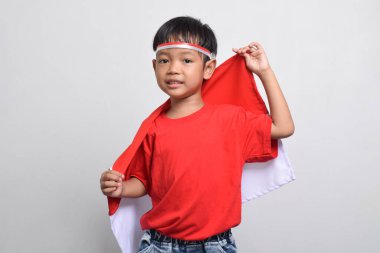 Beyaz arka planda izole edilmiş, arkasında Endonezya bayrağı taşıyan neşeli bir Asyalı çocuk. Endonezya Bağımsızlık Günü konsepti.