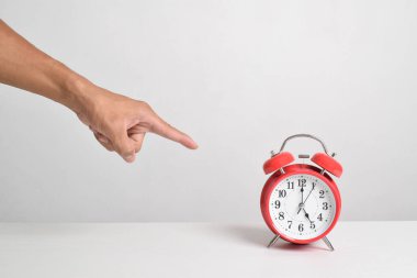 Çalar saati elinde tutup parmağınla gösteriyorsun. Beyaz arka planda, kırmızı alarm saatini elinde tutan adam. Kırpma yolu ile yakın çekim. Zaman kavramı