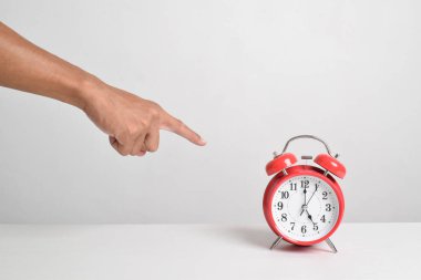 Çalar saati elinde tutup parmağınla gösteriyorsun. Beyaz arka planda, kırmızı alarm saatini elinde tutan adam. Kırpma yolu ile yakın çekim. Zaman kavramı