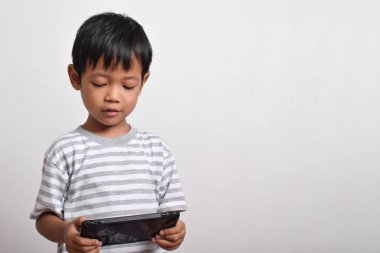 Küçük tatlı Asyalı çocuk beyaz arka planda izole edilmiş akıllı telefonuyla oynuyor. Cep telefonu tutan çocuk. Teknoloji konsepti