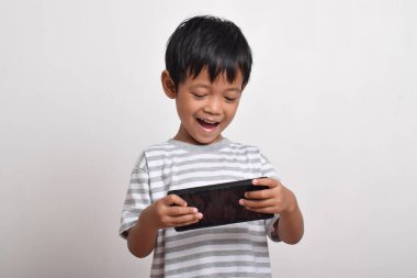 Küçük tatlı Asyalı çocuk beyaz arka planda izole edilmiş akıllı telefonuyla oynuyor. Cep telefonu tutan çocuk. Teknoloji konsepti