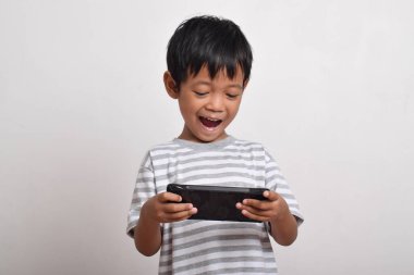 Küçük tatlı Asyalı çocuk beyaz arka planda izole edilmiş akıllı telefonuyla oynuyor. Cep telefonu tutan çocuk. Teknoloji konsepti