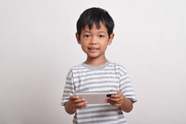 Küçük tatlı Asyalı çocuk beyaz arka planda izole edilmiş akıllı telefonuyla oynuyor. Cep telefonu tutan çocuk. Teknoloji konsepti