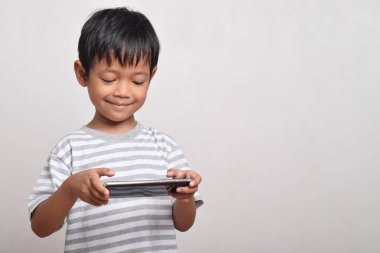 Küçük tatlı Asyalı çocuk beyaz arka planda izole edilmiş akıllı telefonuyla oynuyor. Cep telefonu tutan çocuk. Teknoloji konsepti
