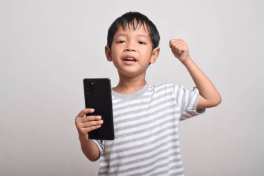 Beyaz arka planda izole edilmiş akıllı telefonu tutan mutlu ve heyecanlı bir Asyalı çocuk. Küçük çocuk telefonu tutuyor. Teknoloji kavramı, kopyalama alanı