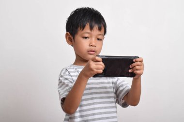 Beyaz arka planda izole edilmiş akıllı telefon oynayan ciddi yüzlü Asyalı bir çocuk. Oyun oynayan küçük bir çocuk. Oyun ve Teknoloji kavramı, kopyalama alanı