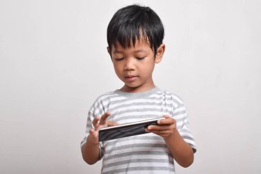 Beyaz arka planda izole edilmiş akıllı telefon oynayan ciddi yüzlü Asyalı bir çocuk. Oyun oynayan küçük bir çocuk. Oyun ve Teknoloji kavramı, kopyalama alanı