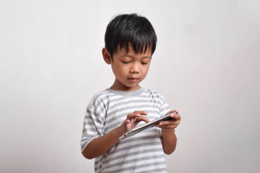 Beyaz arka planda izole edilmiş akıllı telefon oynayan ciddi yüzlü Asyalı bir çocuk. Oyun oynayan küçük bir çocuk. Oyun ve Teknoloji kavramı, kopyalama alanı