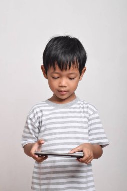 Beyaz arka planda izole edilmiş akıllı telefon oynayan ciddi yüzlü Asyalı bir çocuk. Oyun oynayan küçük bir çocuk. Oyun ve Teknoloji kavramı, kopyalama alanı