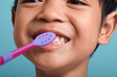 Dişlerini fırçalayan mutlu Asyalı çocuk mavi arka planda izole edilmiş. Çocuk diş sağlığı, tıbbi bakım.