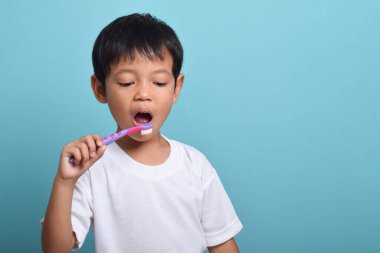 Dişlerini fırçalayan Asyalı çocuk mavi arka planda izole edilmiş. Sağlık, ağız temizliği.
