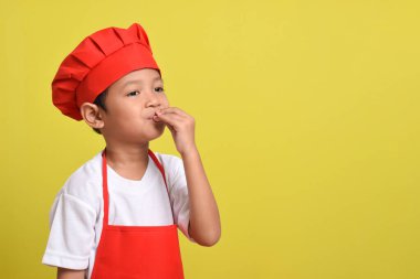 Sarı arka planda mükemmel bir işaret gösteren sevimli bir aşçı. Asyalı çocuk kırmızı önlük ve şapka takıyor. Metin için boşluk