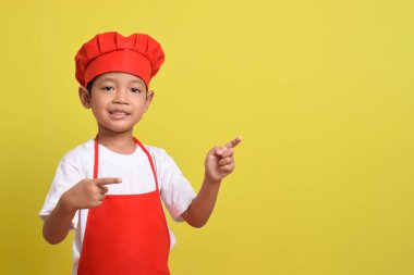 Sarı arka planda, işaret eden el hareketleriyle Boş Alan 'ı gösteren sevimli bir aşçı. Asyalı çocuk kırmızı önlük ve şapka takıyor. Teklif konsepti. Reklam pankartı