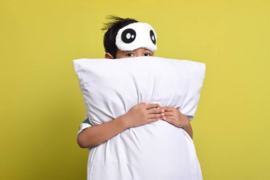 Sarı arka planda, pijama giyen ve uyku maskesi takan sevimli Asyalı bir çocuğun portresi. Sağlıklı uyku konsepti. Boşluğu kopyala