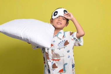 Sarı arka planda izole edilmiş pijama ve uyku maskesi takan neşeli Asyalı çocuk portresi. Sağlıklı uyku konsepti. Boşluğu kopyala