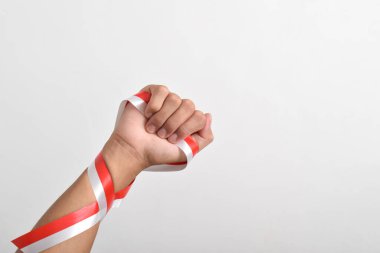 Beyaz zemin üzerinde izole edilmiş kırmızı ve beyaz Endonezya bayrağının sembolü olarak kırmızı ve beyaz kurdeleyi tutan yumruk. 17 Ağustos 'ta Endonezya Bağımsızlık Günü Konsepti. Kopya Boşluğu