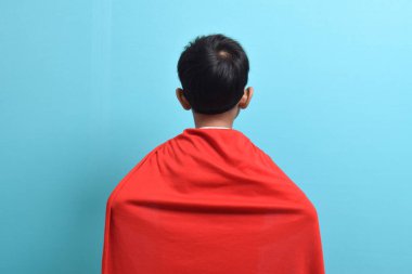 Süper kahraman kostümü giymiş Asyalı bir çocuğun elleri belinde dikilirken mavi arka planda görüntüsü. Başarı ve kazanan konsepti