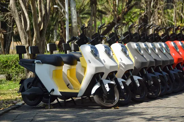 Renkli elektrikli scooterların yan görüntüsü. Şehir parkında arka arkaya park etmiş elektrikli motosikletler.