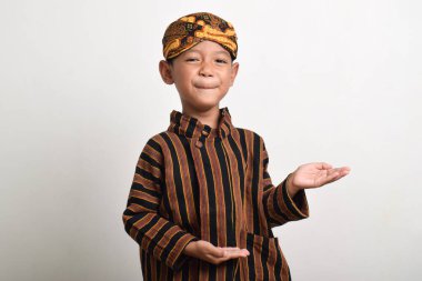 Geleneksel Cava kıyafetleri giyen Asyalı çocuk beyaz arka planda izole edilmiş şekilde gülümsüyor ve el kol hareketi yapıyor. Batik Lurik giyen çocuk.