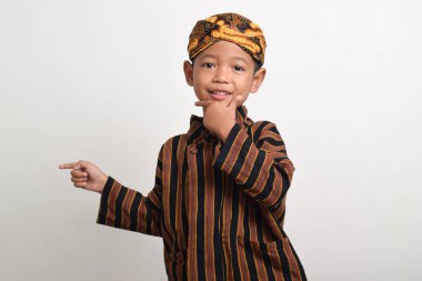 Asian boy wearing traditional Javanese clothes pointing to the right with a smiling expression isolated on white background. Boy wearing Batik Lurik clipart