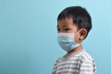 Sağlık maskesi takan Asyalı çocuk mavi arka planda izole edilmiş. Tıbbi ve sağlık konsepti. İnsan nüfusu virüsleri, enfeksiyonlar, grip hastalıklarının önlenmesi