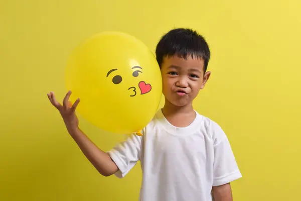 Öpücük emojisi. Sarı arka planda öpüşme balonu tutan yakışıklı Asyalı çocuk.