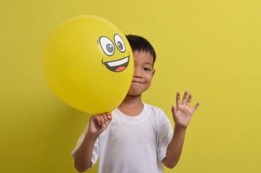 Mutlu emoji. Sarı arka planda neşeli bir balon tutan sevimli Asyalı çocuk.