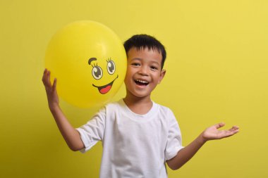 Gülümse emoji. Sarı arka planda mutlu bir balon tutan sevimli Asyalı çocuk.