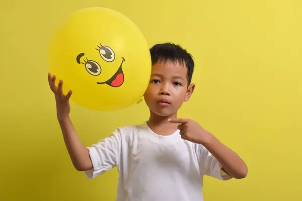 Gülümse emoji. Sarı arka planda mutlu bir balon tutan sevimli Asyalı çocuk.