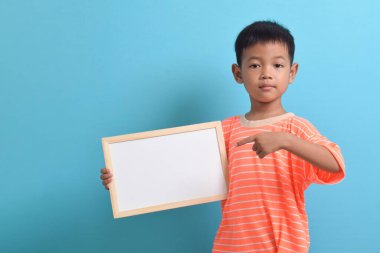 Mavi arka planda boş bir tahta tutan sevimli küçük Asyalı çocuk. Metin, kopyalama alanı, biçimlendirme pankartı için boşluk