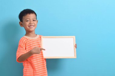 Mavi arka planda boş bir tahta tutan sevimli küçük Asyalı çocuk. Metin, kopyalama alanı, biçimlendirme pankartı için boşluk