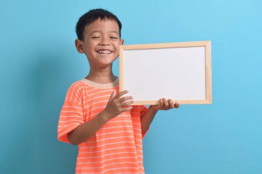 Mavi arka planda boş bir tahta tutan sevimli küçük Asyalı çocuk. Metin, kopyalama alanı, biçimlendirme pankartı için boşluk