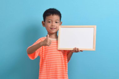Mavi arka planda boş bir tahta tutan sevimli küçük Asyalı çocuk. Metin, kopyalama alanı, biçimlendirme pankartı için boşluk