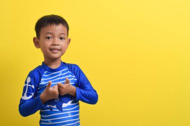 Mayo giyen şirin bir Asyalı çocuğun portresi sarı arka planda izole edilmiş başparmakları gösteriyor. Yaz tatili kavramı. Kopyalama uzayıyla