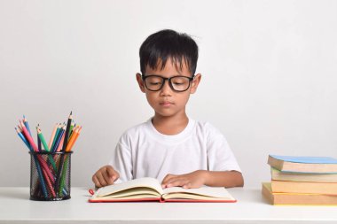 Asyalı bir çocuğun portresi beyaz arka planda izole edilmiş bir kitaba ciddi ciddi bakıyor.