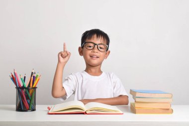 Beyaz bir arka planda izole edilmiş Asyalı bir çocuğun portresi. Bir soruya cevap vermek için elini kaldırıyor.