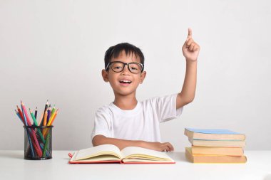 Beyaz bir arka planda izole edilmiş Asyalı bir çocuğun portresi. Bir soruya cevap vermek için elini kaldırıyor.