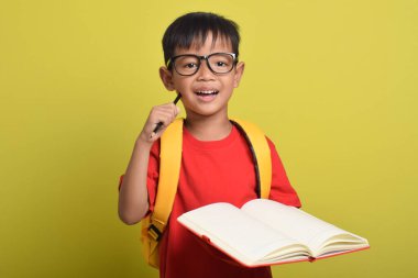 Sırt çantasında kalem tutan Asyalı bir çocuğun portresi ve sarı arka planda izole edilmiş düşünce problemi. Ders çalışma zamanı. Okula geri dön.