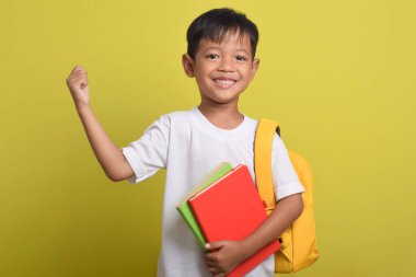 Sırt çantalı gülümseyen Asyalı çocuk, kazanan jest, başarıyı kutlayan, sarı arka planda izole edilmiş. Okul konseptine geri dönelim. Boşluğu kopyala