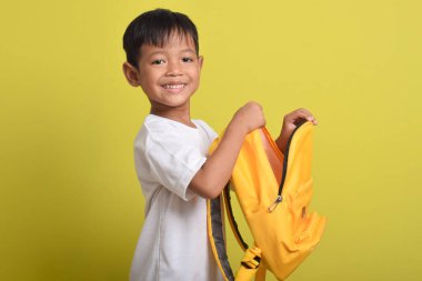 Sarı arka planda, sırt çantasının açık duran neşeli Asyalı çocuğun portresi. Okul için hazırlık. Kameraya bakıyorum. Okul konseptine dönüş