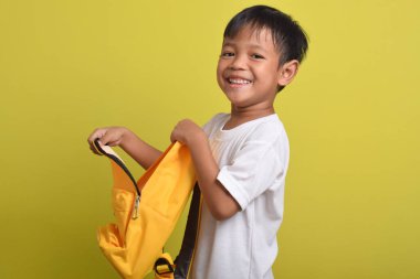 Sarı arka planda, sırt çantasının açık duran neşeli Asyalı çocuğun portresi. Okul için hazırlık. Kameraya bakıyorum. Okul konseptine dönüş