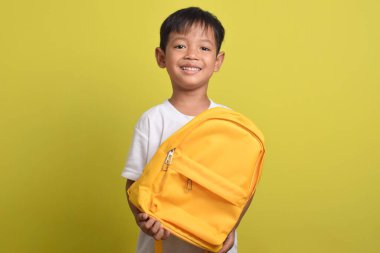 Sarı arka planda izole edilmiş okul çantası tutan mutlu bir Asyalı çocuk. Çalışmaya hazırlanan sevimli bir çocuk. Okul konseptine dönüş