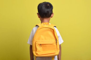 Sarı arka planda sarı sırt çantalı Asyalı çocuğun arka planı. Eğitim konsepti. Okula geri dön.