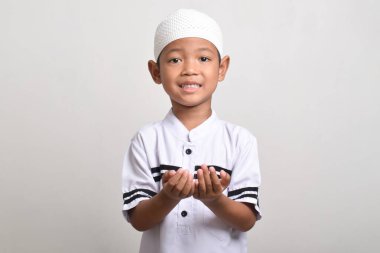 Asyalı Müslüman çocuk beyaz arka planda elleri açık dua ediyor. Tanrı 'ya dua ediyorum, dua ediyorum, ellerim havada.