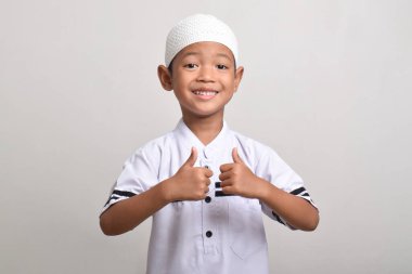 Portrait of a Muslim Asian boy smiling happily and giving a thumbs up isolated on a white background. clipart